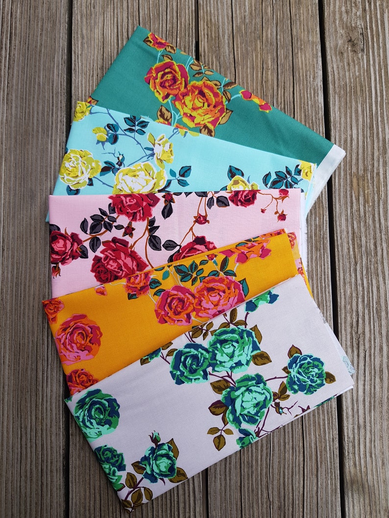 May include: Six fabric swatches with floral patterns featuring roses in various colors, including pink, red, orange, yellow, teal, and green. The fabric swatches are arranged in a fan shape on a wooden surface.