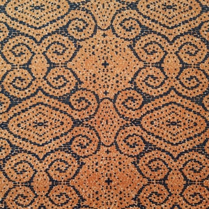 Könnte beinhalten: Nahaufnahme eines strukturierten Stoffes mit sich wiederholendem Muster. Das Design zeigt dunkelmarineblaue Formen auf einem warmen orangebraunen Hintergrund. Das Muster umfasst Wirbel, Rauten und Punktcluster, wodurch ein detailliertes Textil entsteht.