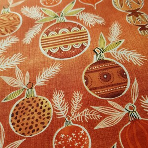 May include: Orange fabric with a repeating pattern of stylized Christmas ornaments. The ornaments are in shades of brown, orange, and yellow with various patterns.