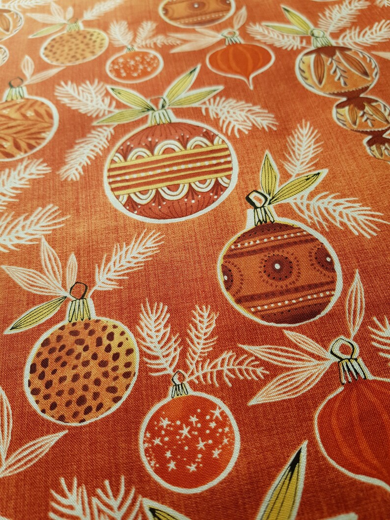 May include: Orange fabric with a repeating pattern of stylized Christmas ornaments. The ornaments are in shades of brown, orange, and yellow with various patterns.