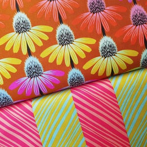 May include: Close-up of two fabric patterns. The top pattern features large, stylized flowers in yellow, orange, pink, and black on an orange background. The bottom pattern has diagonal stripes in pink, yellow, and light blue.