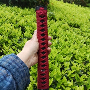 May include: A red and black sword handle with a diamond pattern. The handle is wrapped in a red cord and has a black tassel at the top.