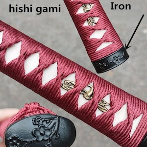 May include: Close-up of a katana handle with a burgundy wrap and white diamond-shaped accents. The handle features gold-coloured metal ornaments and black iron fittings with floral designs. The text "hishi gami" is visible.