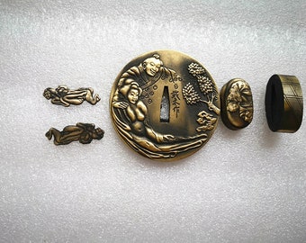 May include: A set of four gold-toned metal Japanese sword fittings, or tsuba, featuring a decorative design of a couple embracing. The tsuba are intricately detailed and include a small tree and a Japanese character.