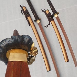 May include: Four Japanese katana swords with brown handles and wooden blades. The scabbards are gold and brown, with decorative metal fittings. The swords are arranged diagonally on a light background, showcasing their craftsmanship.