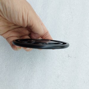 Op de afbeelding: Zwarte ronde onderzetter met een reliëfdesign. De onderzetter is gemaakt van een hard, duurzaam materiaal.
