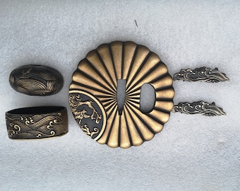 May include: A set of four gold and black Japanese sword fittings, or tsuba, featuring a wave design. The tsuba are made of metal and have a traditional Japanese style.