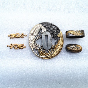 May include: A collection of Japanese sword fittings, including a tsuba, fuchi, kashira, and two kozuka. The tsuba showcases a detailed dragon and koi fish design in gold and black. The other fittings also feature dragon motifs.