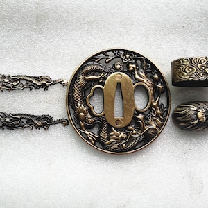 May include: A set of four gold-toned metal sword fittings, including a tsuba (sword guard) with a dragon design, a fuchi (collar) with a cloud design, a kashira (pommel cap) with a lion design, and two dragon-shaped seppa (spacer).