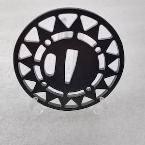 Op de afbeelding: Een zwarte ronde onderzetter met een decoratief ontwerp van driehoeken rond de rand. Het midden van de onderzetter heeft een zwarte cirkel met een wit nummer "1" erin.
