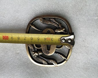 May include: A gold-coloured metal sword guard with a dragonfly design. The guard is 9.5 cm in diameter and has a circular opening in the centre.