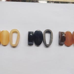 May include: A collection of various oval and rounded jewelry components in shades of yellow, black, and brown. The components include solid ovals, open ovals, and a dark oval with a rounded top. The components are arranged in a row.