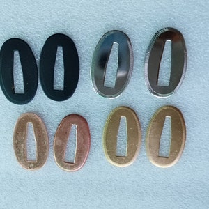 May include: Six oval-shaped metal pieces with a rectangular hole in the center. The pieces are in three different colors: black, silver, and gold.