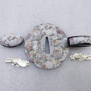 Op de afbeelding: Een set van vijf decoratieve Japanse zwaardbeslag, of tsuba, gemaakt van metaal en ingelegd met parelmoer. De tsuba zijn in verschillende vormen en maten en hebben ingewikkelde ontwerpen van bloemen en andere motieven. De tsuba zijn een prachtig voorbeeld van Japans vakmanschap.