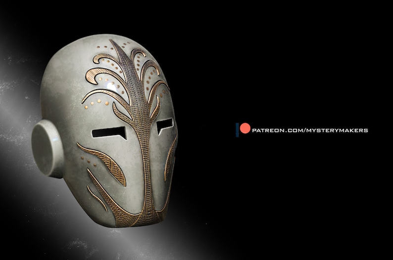 Op de afbeelding: Een zilveren en gouden masker met ingewikkelde ontwerpen. Het masker heeft een gestileerd gezicht met twee ooggaten en een klein oorstuk aan de zijkant.