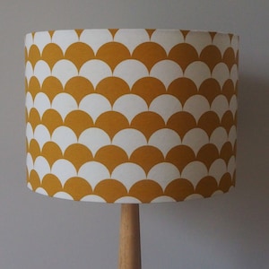 May include: A yellow and white lampshade with a geometric pattern of overlapping half circles. The lampshade is made of fabric and has a cylindrical shape.