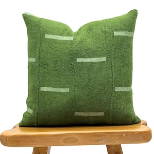 May include: A green throw pillow with white stripes on a wooden stool. The pillow is made of a textured fabric and has a simple, modern design.