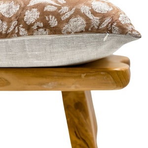 May include: A brown and white floral patterned pillow with a zipper closure sits on a wooden stool.