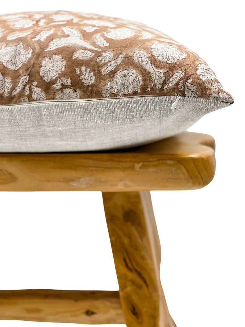 May include: A brown and white floral patterned pillow with a zipper closure sits on a wooden stool.