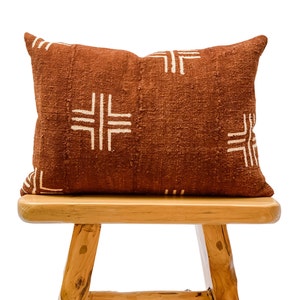 May include: A brown throw pillow with a white geometric pattern. The pillow is sitting on a wooden stool.