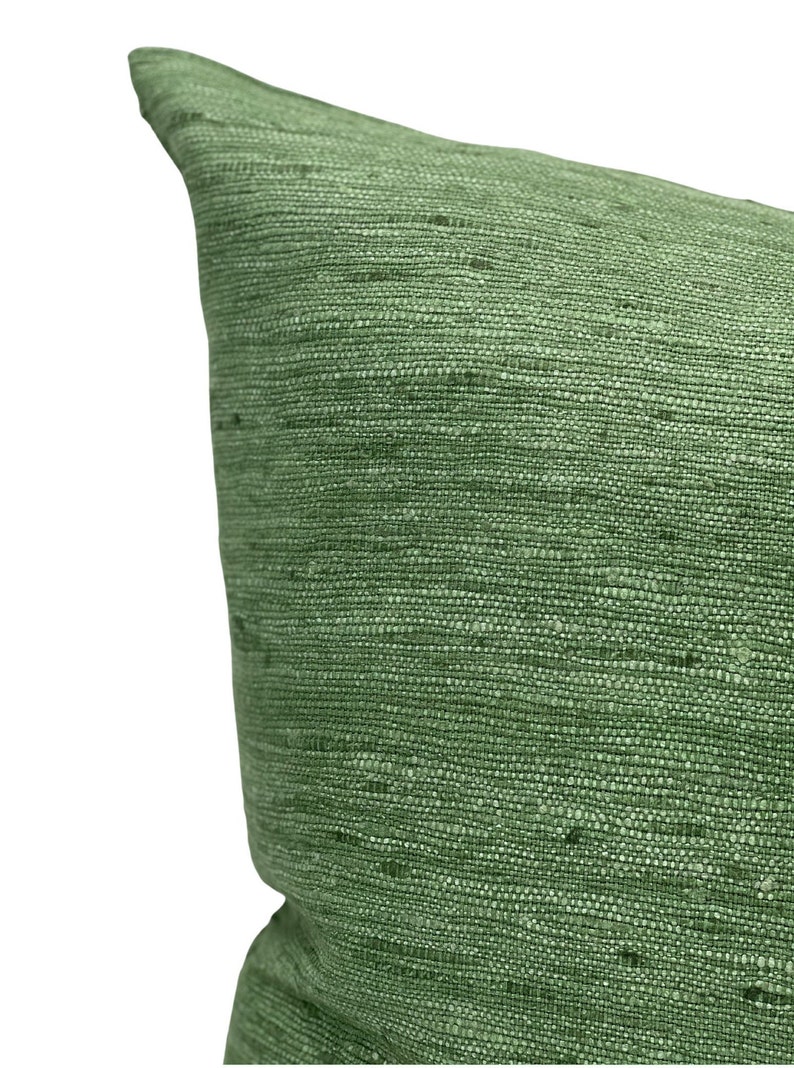 Puede incluir: Una almohada verde con una tela texturizada. La almohada est&aacute; hecha de un material tejido con un brillo sutil.