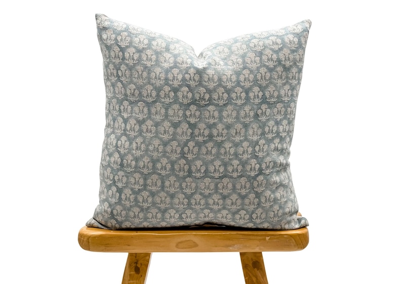 May include: A blue throw pillow with a white floral pattern. The pillow is sitting on a wooden stool.