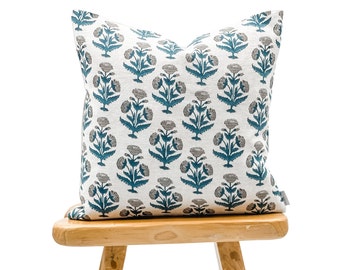 May include: A teal and white floral patterned throw pillow on a wooden stool.