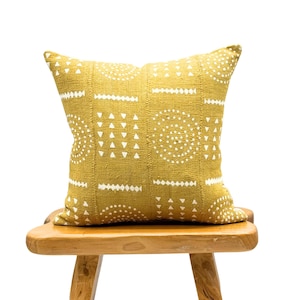 May include: A mustard yellow throw pillow with a white geometric pattern. The pillow is sitting on a wooden stool.