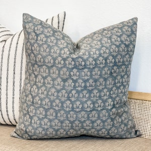 May include: A blue throw pillow with a white floral pattern. The pillow is sitting on a light brown couch.