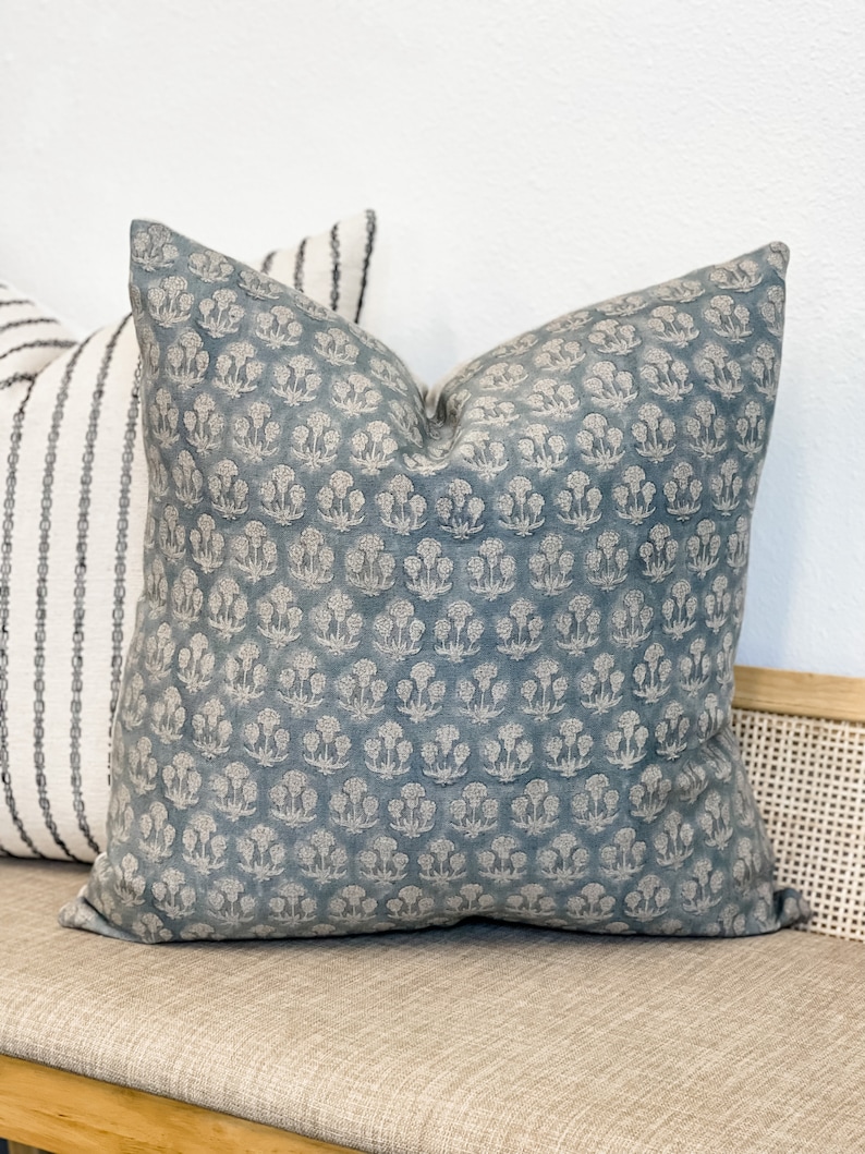 May include: A blue throw pillow with a white floral pattern. The pillow is sitting on a light brown couch.