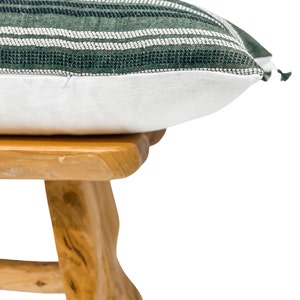 Pode incluir: Uma almofada decorativa com um padr&atilde;o listrado verde e branco na parte superior e uma parte inferior branca. A almofada est&aacute; sobre um pequeno banco de madeira clara.