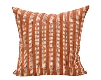May include: A terracotta-colored throw pillow with a white geometric pattern. The pillow has a square shape and is made of a soft, textured fabric.