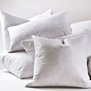 May include: A set of four white down pillows of varying sizes. The pillows are arranged in a pyramid shape, with the largest pillow at the bottom and the smallest pillow at the top.