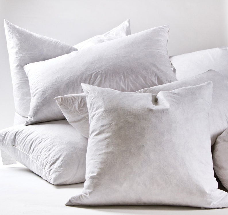 May include: A set of four white down pillows of varying sizes. The pillows are arranged in a pyramid shape, with the largest pillow at the bottom and the smallest pillow at the top.
