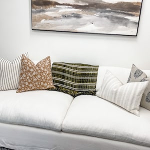 May include: A white sofa with a variety of throw pillows and a green and black plaid throw blanket. The pillows are striped, patterned, and solid.