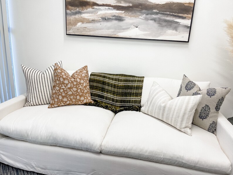 May include: A white sofa with a variety of throw pillows and a green and black plaid throw blanket. The pillows are striped, patterned, and solid.