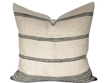 Puede incluir: Una almohada blanca con rayas horizontales negras. La almohada está hecha de una tela suave y texturizada.