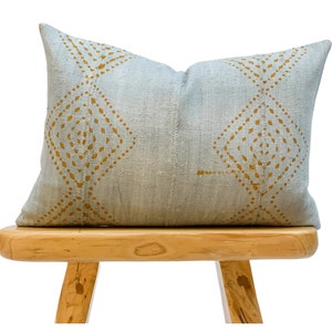 May include: A light blue throw pillow with a geometric pattern in a mustard yellow color. The pillow is sitting on a wooden stool.