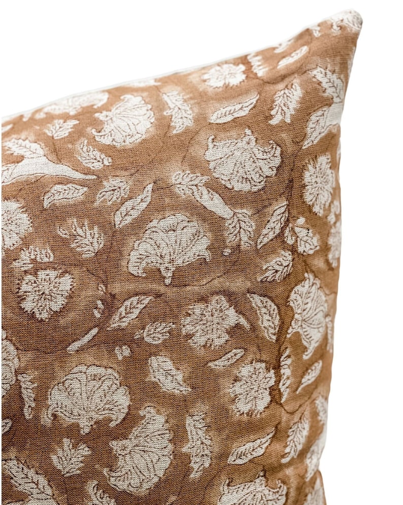 May include: A brown throw pillow with a white floral pattern. The pillow is made of a soft, textured fabric.