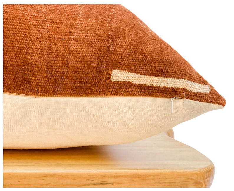 May include: A rust-colored throw pillow with a white stripe across the front. The pillow is made of a woven fabric and has a zipper closure.