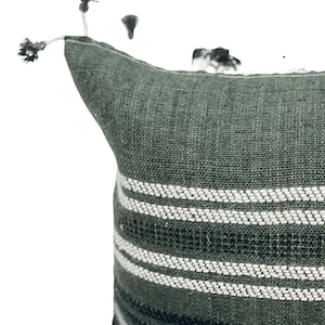 Pode incluir: Uma almofada decorativa verde escuro com listras horizontais brancas. A almofada tem um tecido texturizado e &eacute; adornada com pequenas borlas no canto. Esta almofada de acento &eacute; adequada para uma cama ou sof&aacute;.