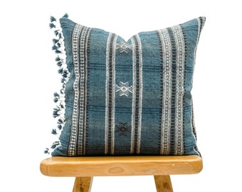 May include: A blue and white striped cushion with fringe trim. The cushion is made of a woven fabric and has a geometric pattern.