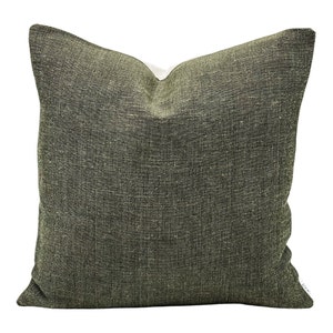 May include: Square decorative pillow with a textured, olive green fabric cover. The pillow has a neutral-colored backing and a visible seam. The fabric has a woven appearance, adding visual interest to the design. The pillow is suitable for home decor.