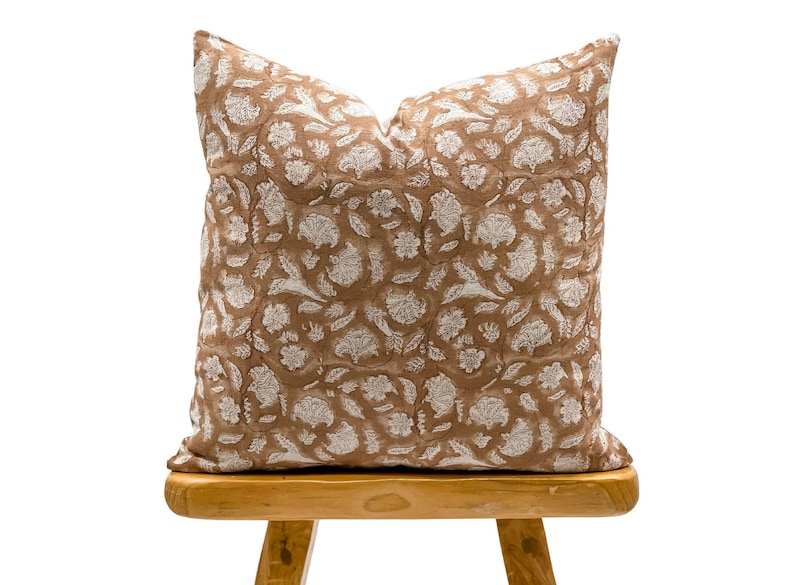 May include: A brown throw pillow with a white floral pattern. The pillow is sitting on a wooden stool.