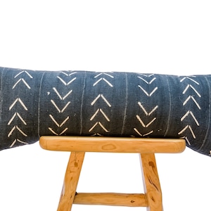 May include: A long, blue and white patterned bolster pillow with a white chevron design. The pillow is resting on a wooden stool.