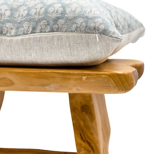 May include: A light blue floral patterned pillow with a zipper closure sits on top of a wooden stool with a natural finish.