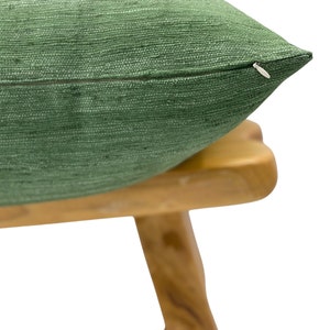 Puede incluir: Una almohada verde con cierre de cremallera, apoyada en un taburete de madera.