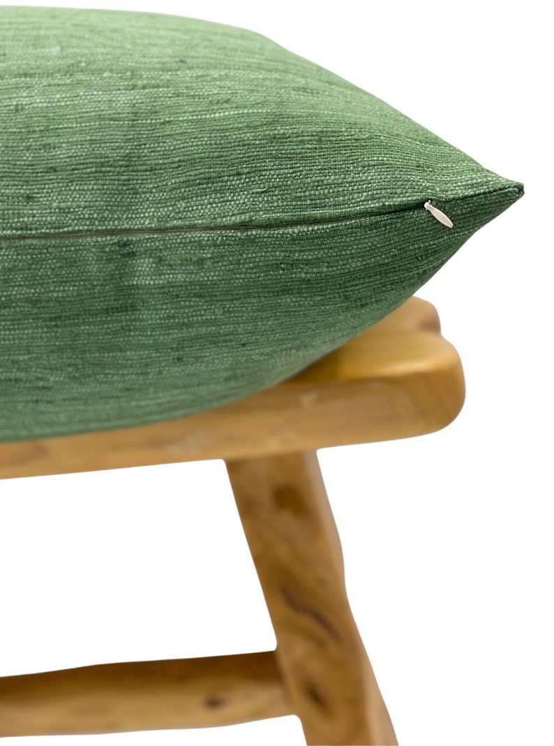 Puede incluir: Una almohada verde con cierre de cremallera, apoyada en un taburete de madera.