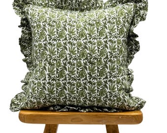 Könnte beinhalten: Ein grünes Kissen mit weißem Blumenmuster und einem Rüschenrand. Das Kissen liegt auf einem Holzhocker.