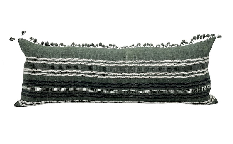 Pode incluir: Uma almofada decorativa longa e retangular em tons de verde, branco e preto. A almofada apresenta listras horizontais e &eacute; adornada com pequenas borlas ao longo da borda superior. A almofada &eacute; projetada para decora&ccedil;&atilde;o de casa.